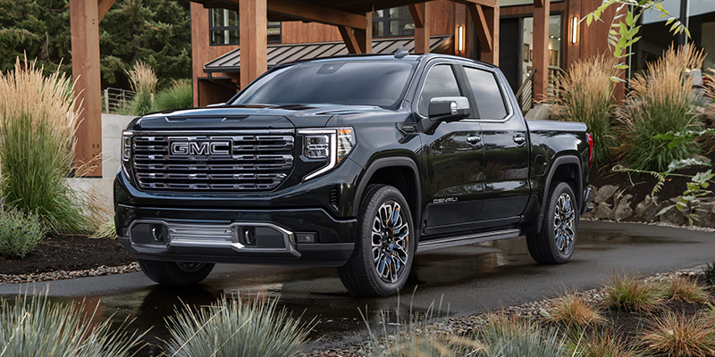 A black 2026 GMC Sierra 1500 parked in a driveway beside a lovely modern desert home and garden