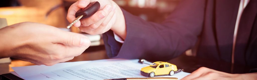 A tiny yellow toy car sits on the financing papers while the close-up view shows GMC SUV sales professional gives the keys to the vehicle to its new owner